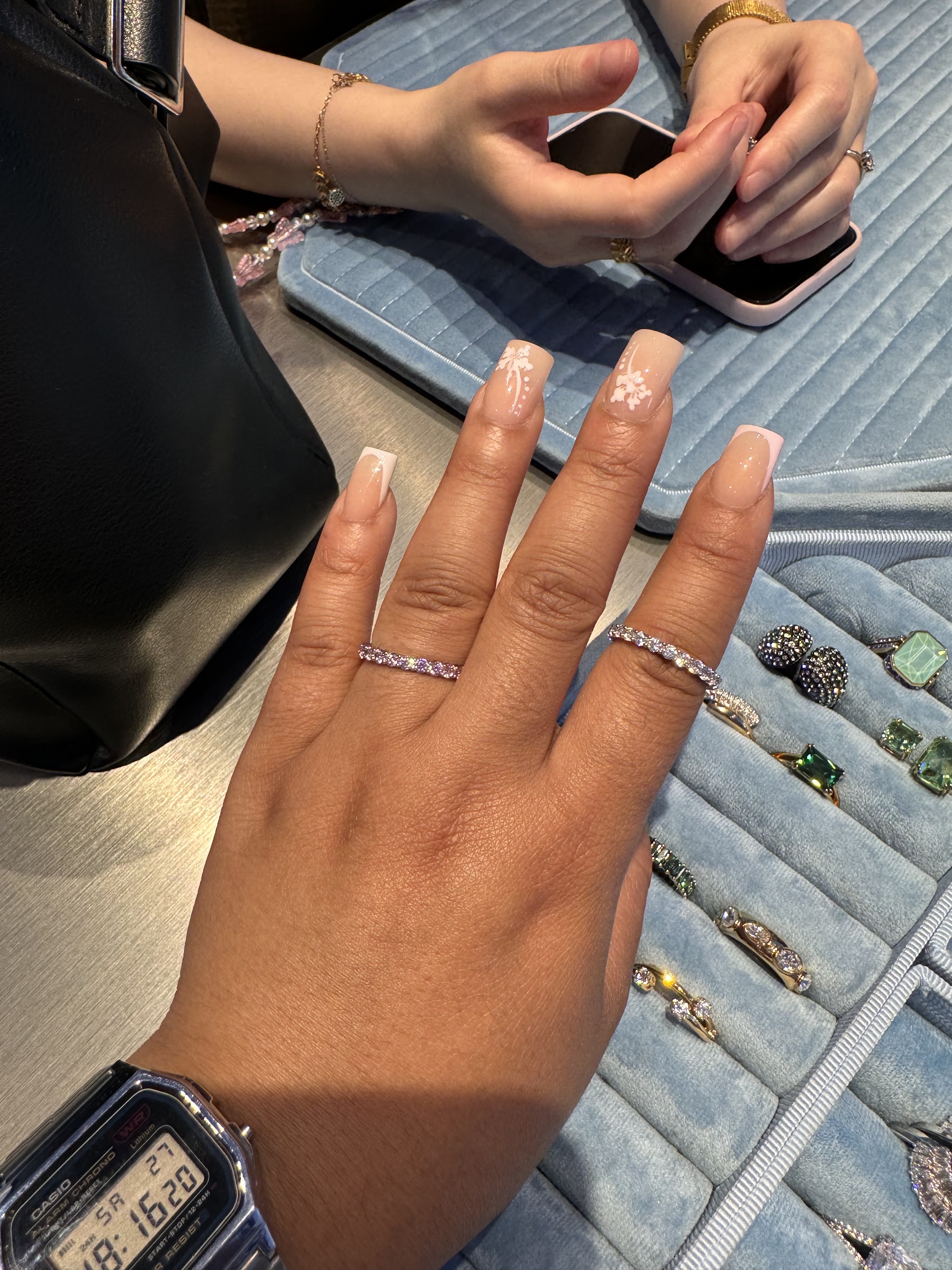 Een hand met natuurlijke French nagels en ringen boven een sieradenbakje